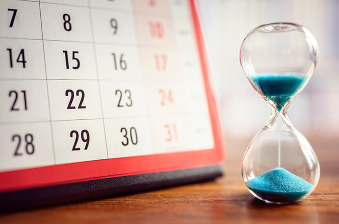 Hourglass with blue sand in front of a calendar