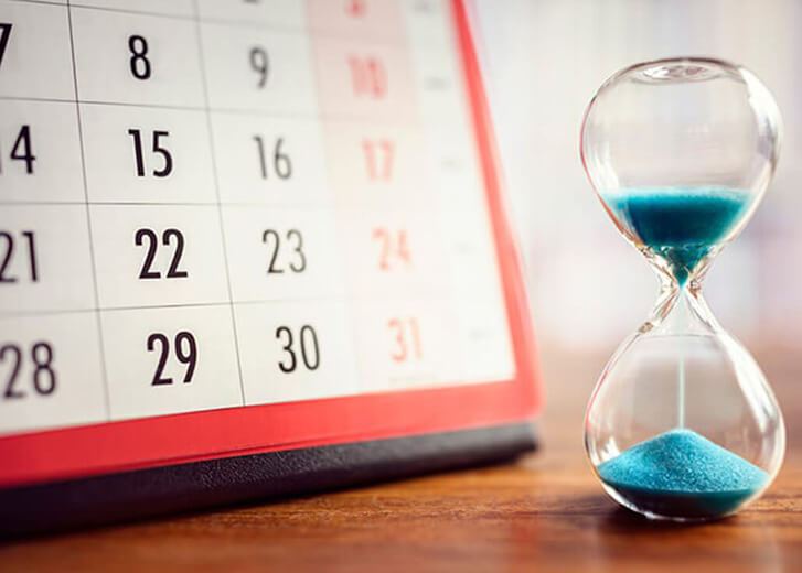 Hourglass with blue sand in front of a calendar