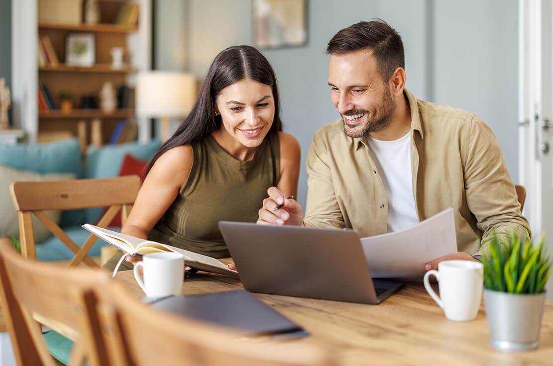 Married couple sit at a table in the living room with laptop,working from home office. Online meeting.