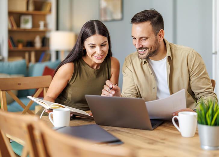 Married couple sit at a table in the living room with laptop,working from home office. Online meeting.